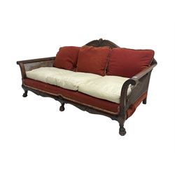 Early 20th century bergère three seat settee, shaped shell carved cresting rail, double caned back and sides, scrolled upright arms and shaped apron carved with shell and foliage, on hairy paw carved feet