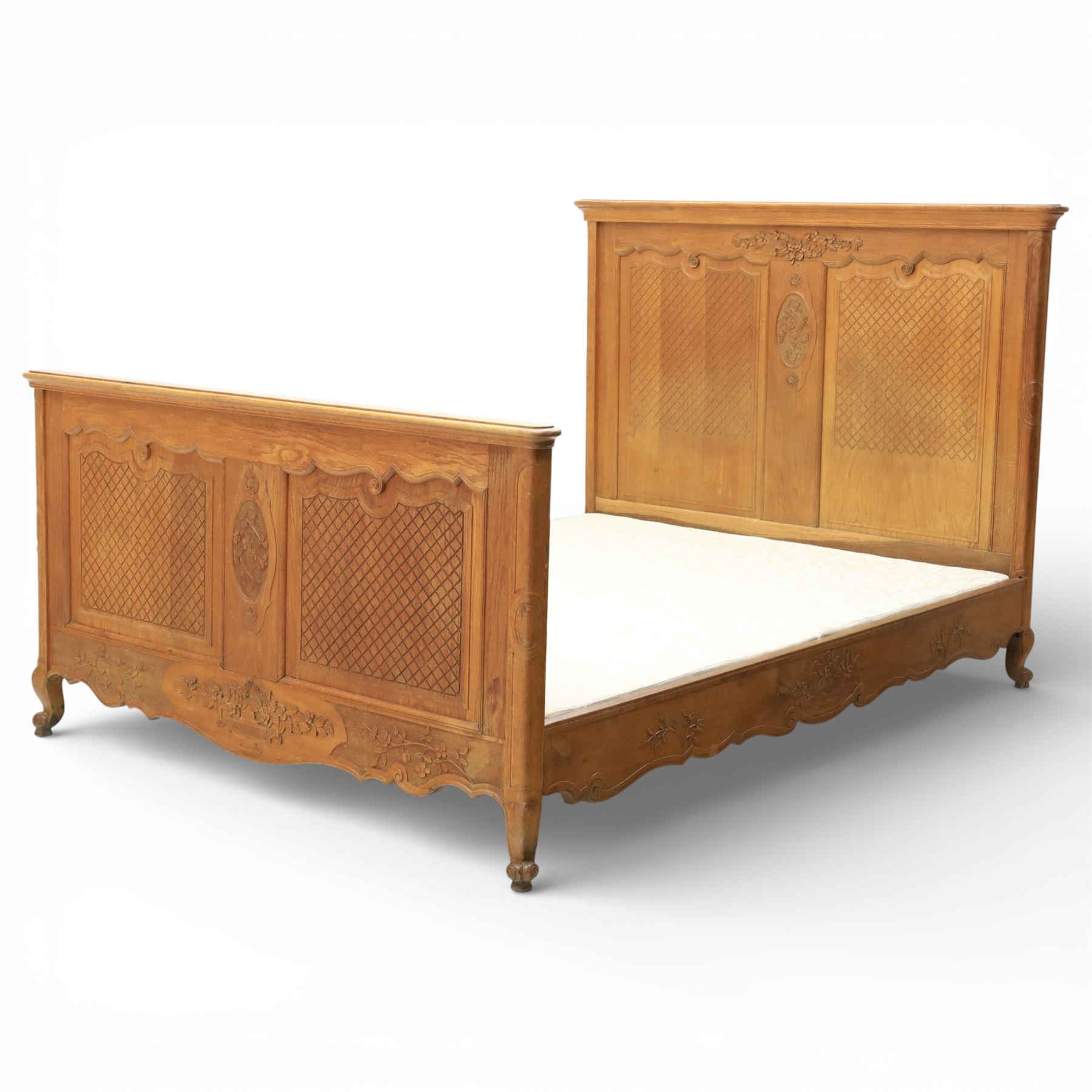Early 20th century French oak double bedstead, the shaped and moulded headboard carved with central floral cartouche and scrolling foliage above lattice carved panels, the conforming footboard with pierced and carved decoration, shaped apron with foliate carving, raised upon cabriole supports