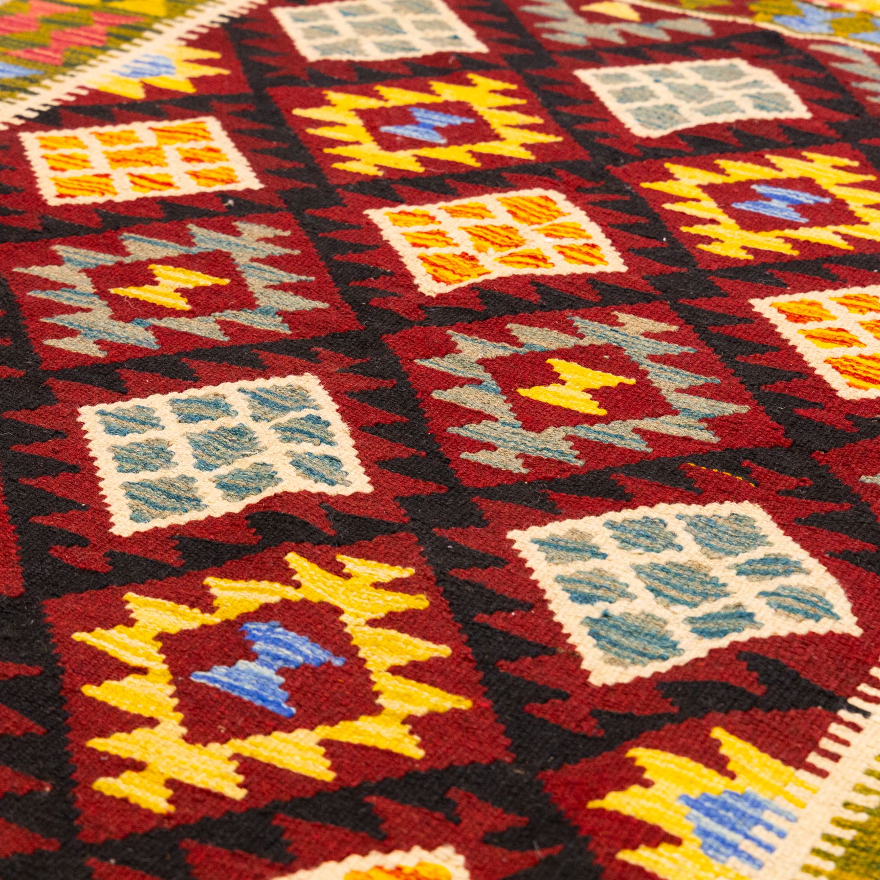 Afghan Maimana flatweave kilim, central crimson field features a large bold nested diamond motif and stylized geometric lozenge patterns on olive purple, blue, yellow and green tone ground, border stripe in teal ground, and fringe