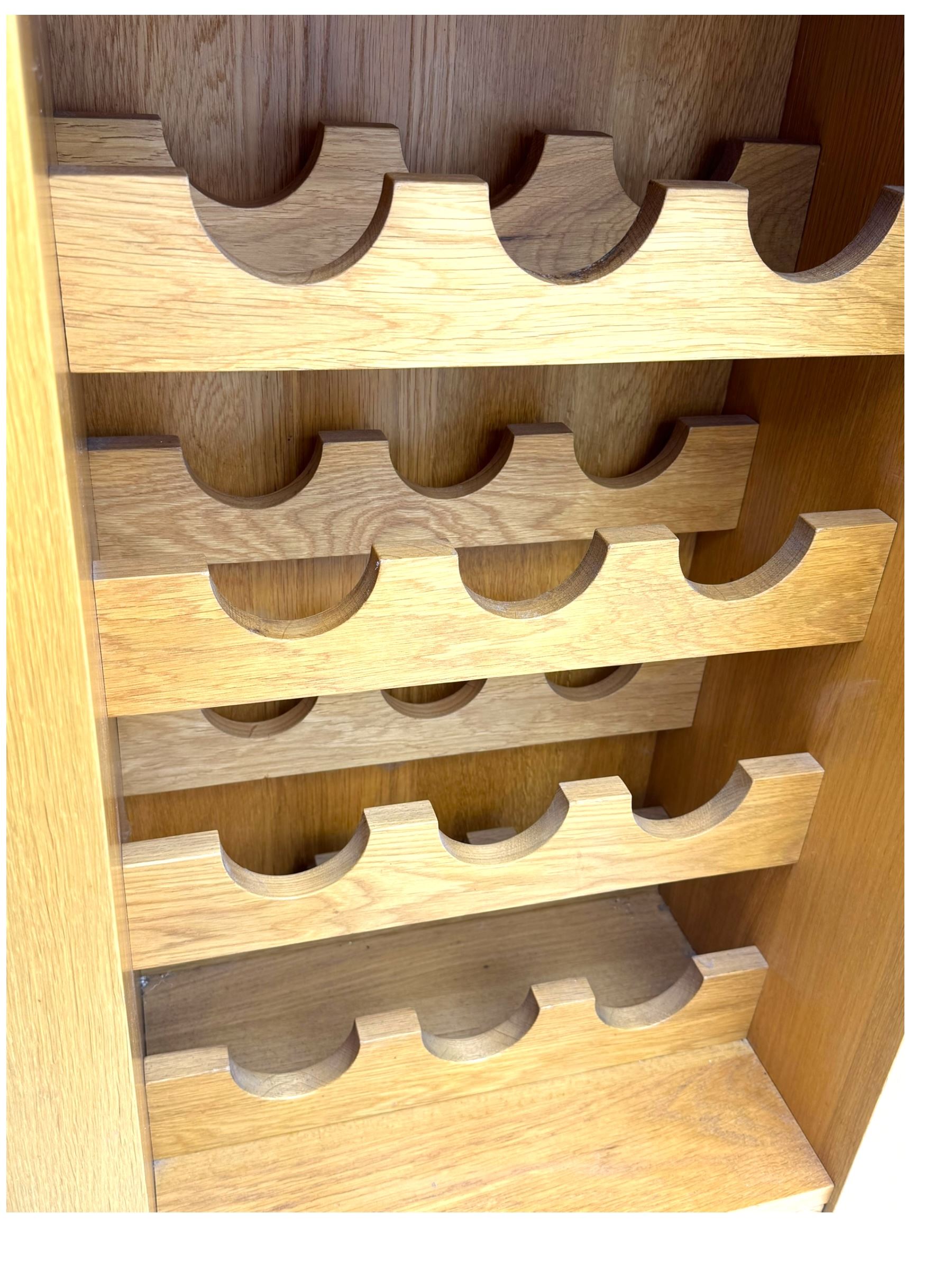 Contemporary light oak wine cabinet, rectangular overhanging top above an open shelf, fitted with four bottle racks each holding three bottles, single drawer with curved metal handle, on chamfered supports