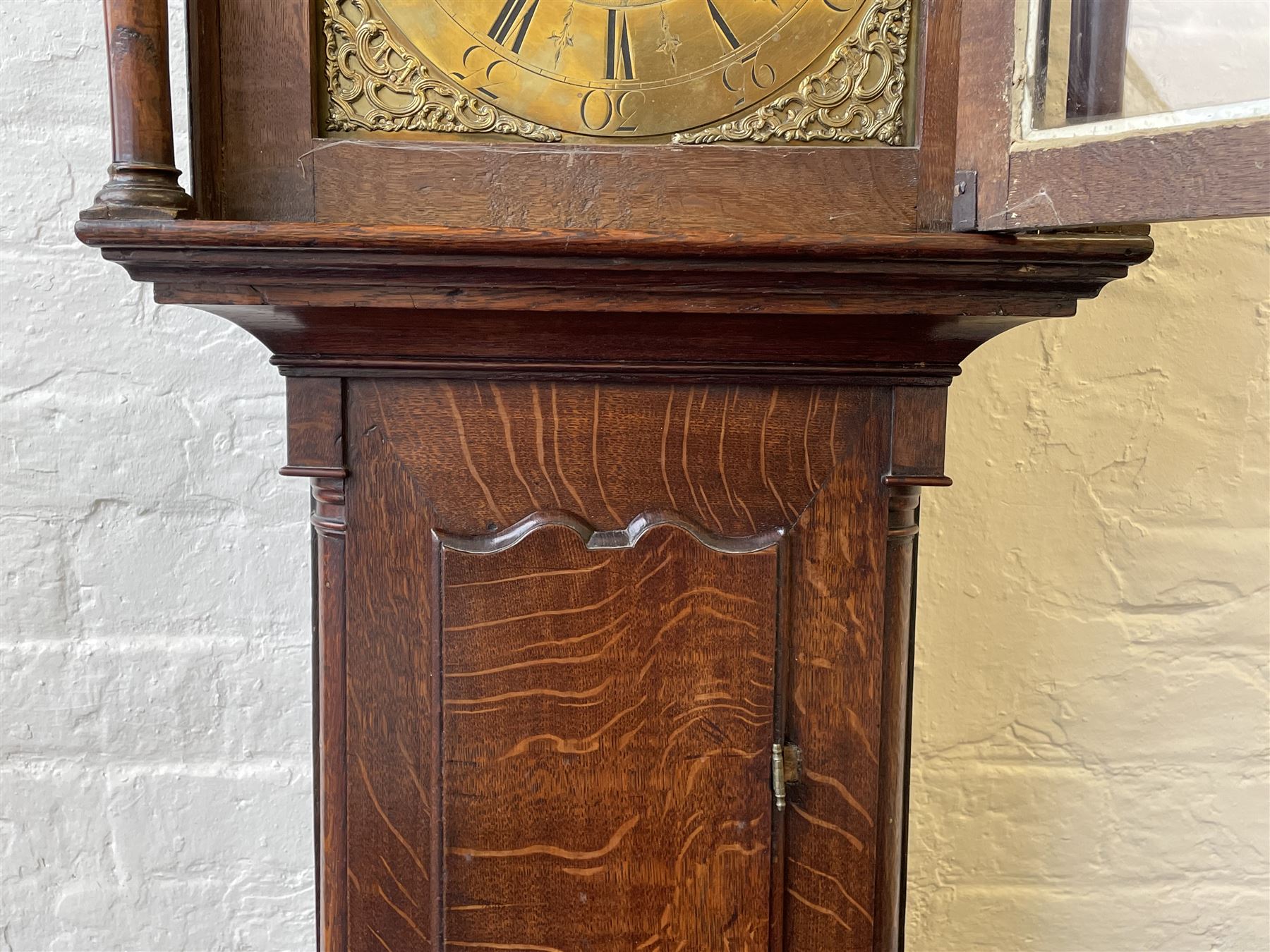 18th century c1760 oak cased George III longcase clock by William Eastwood of Burnley, with a stepped caddy top on a projecting cornice and blind frieze, square glazed door flanked by two turned pillars with gesso capitals, trunk with conforming recessed pillars and a full length wavy topped door, on a square plinth with a raised panel and shaped skirting, 12” square brass dial, 11” chapter ring with Roman numerals and five-minute Arabic's,  