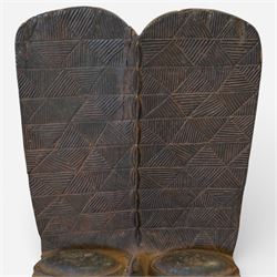African carved hardwood ceremonial seat, monoxylous construction with twin dished seat wells, the tall back incised with repeating geometric triangular motifs, the front carved in the form of a tribal mask with projecting features, raised on a cylindrical base with ribbed and textured carving