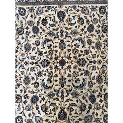 Central Persian Kashan hand-knotted carpet, ivory field with an all-over design of scrolling vines, lotus palmettes, and rosettes in shades of blue and brown within a blue ground border of palmettes and arabesques between multiple guard stripes, 
348 cm x 246cm