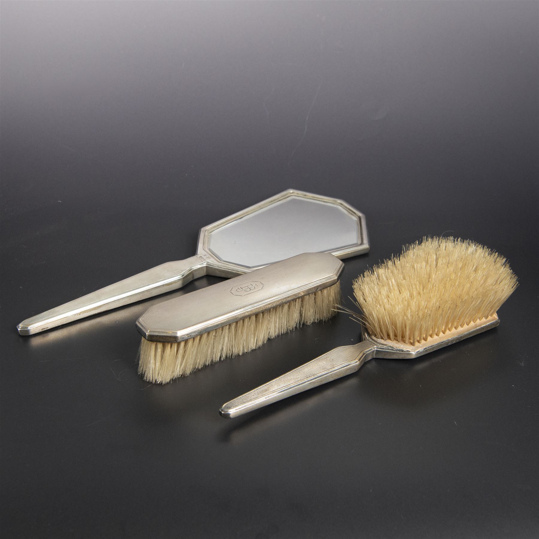 1930s silver mounted three piece dressing table set, comprising hand mirror, hair brush and clothes brush, hallmarked Barker Brothers Silver Ltd, Birmingham 1931