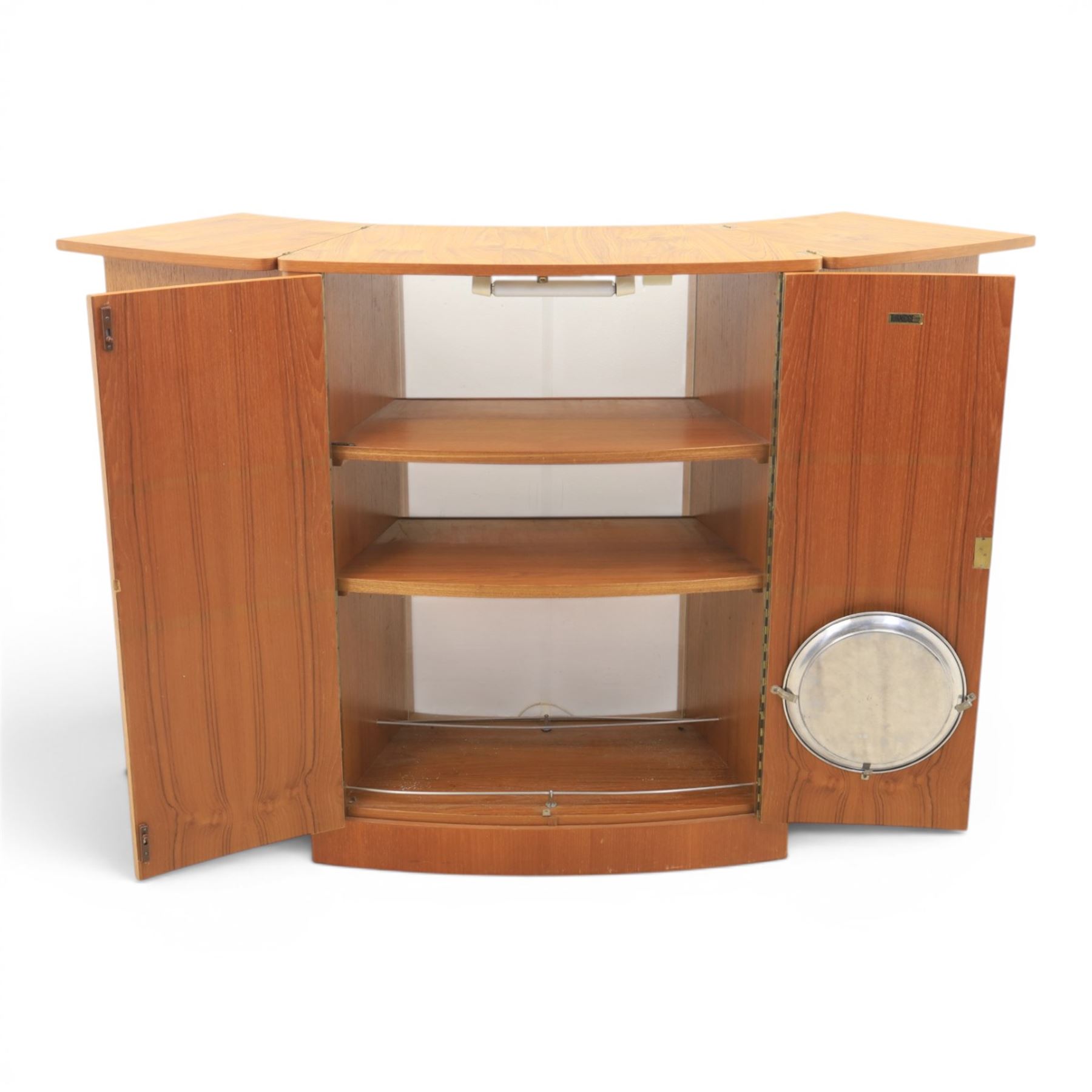Turnidge of London - Mid 20th century teak drinks cabinet, shaped top with hinged fold-out side sections, twin doors with recessed handles enclosing fitted shelving and serving surfaces, sliding glass doors to the back, on a plinth base above castors