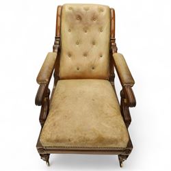 William IV mahogany gentleman's library reclining armchair, leather button upholstered and brass-studded back and seat, above leather-covered arms terminating with carved roundels and foliate scroll-carved ends, underside with brass mechanical trigger reclining lever, the apron with retractable foot rest, supported on lappet carved and turned legs with brass castors, circa 1835