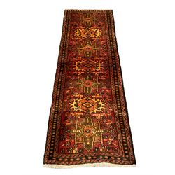 Persian Heriz red ground rug, the field decorated with seven geometric medallions, the field decorated with small stylised motifs of flower heads, repeating three-band border