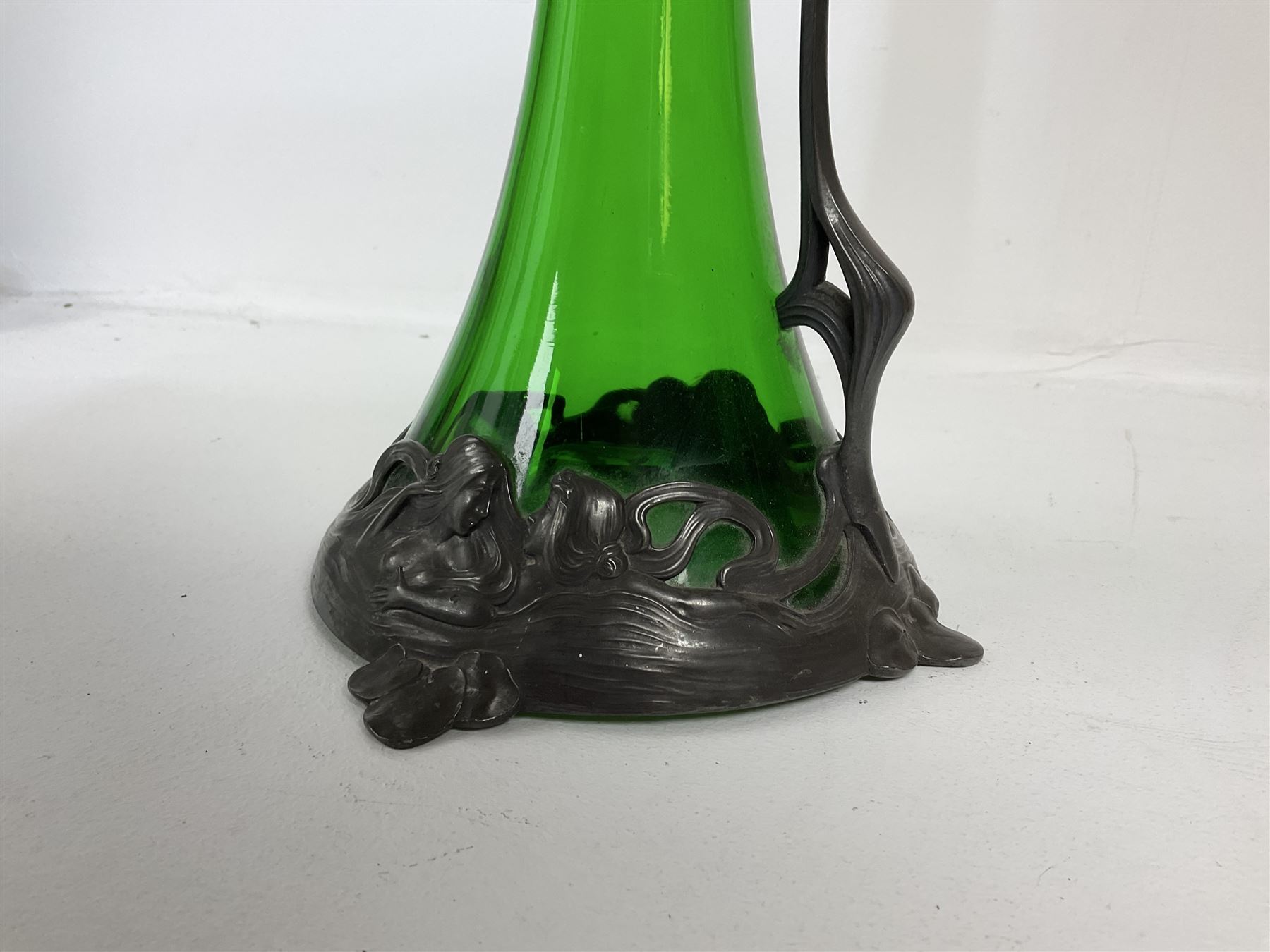 Early 20th century WMF Art Nouveau pewter and green glass ewer, of swept cylindrical form, having a pierced stopper and handle of entwined stems and berry design, the base cast as water nymphs with flowing hair and lily pads, H38cm