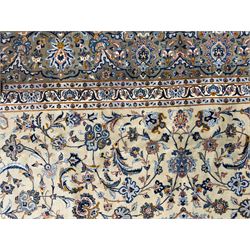 Central Persian Kashan hand-knotted carpet, ivory field with scrolling vines, palmettes, and rosettes around a cusped medallion with pendants and spandrels within a blue ground border of palmettes and flowerheads, 388cm x 300cm