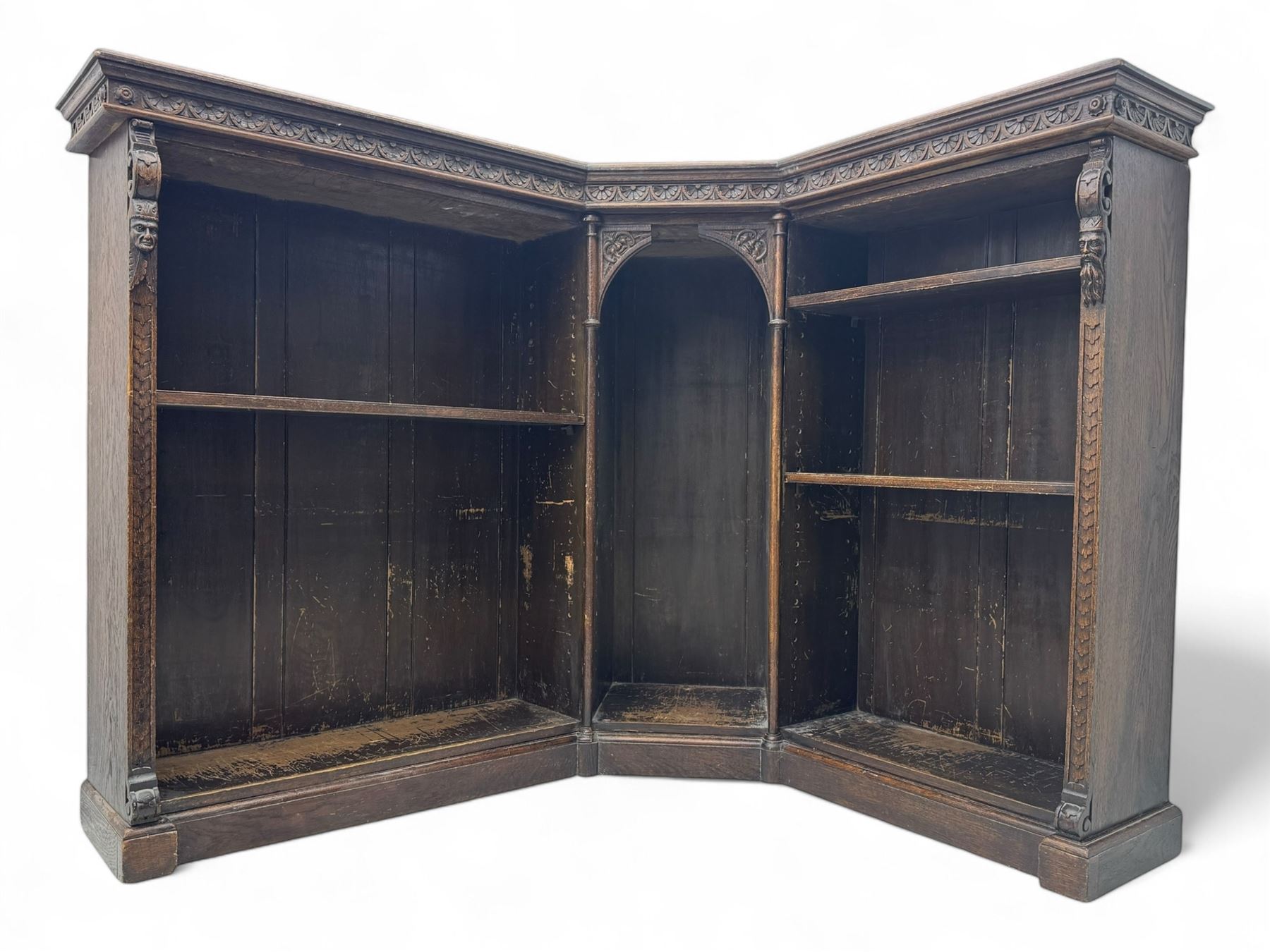 Victorian carved oak corner bookcase, L-shaped form, moulded top over lunette carved frieze, decorated with S-scroll and mask carved corbels with trailing acanthus leaves, fitted with adjustable shelves, on moulded plinth base 