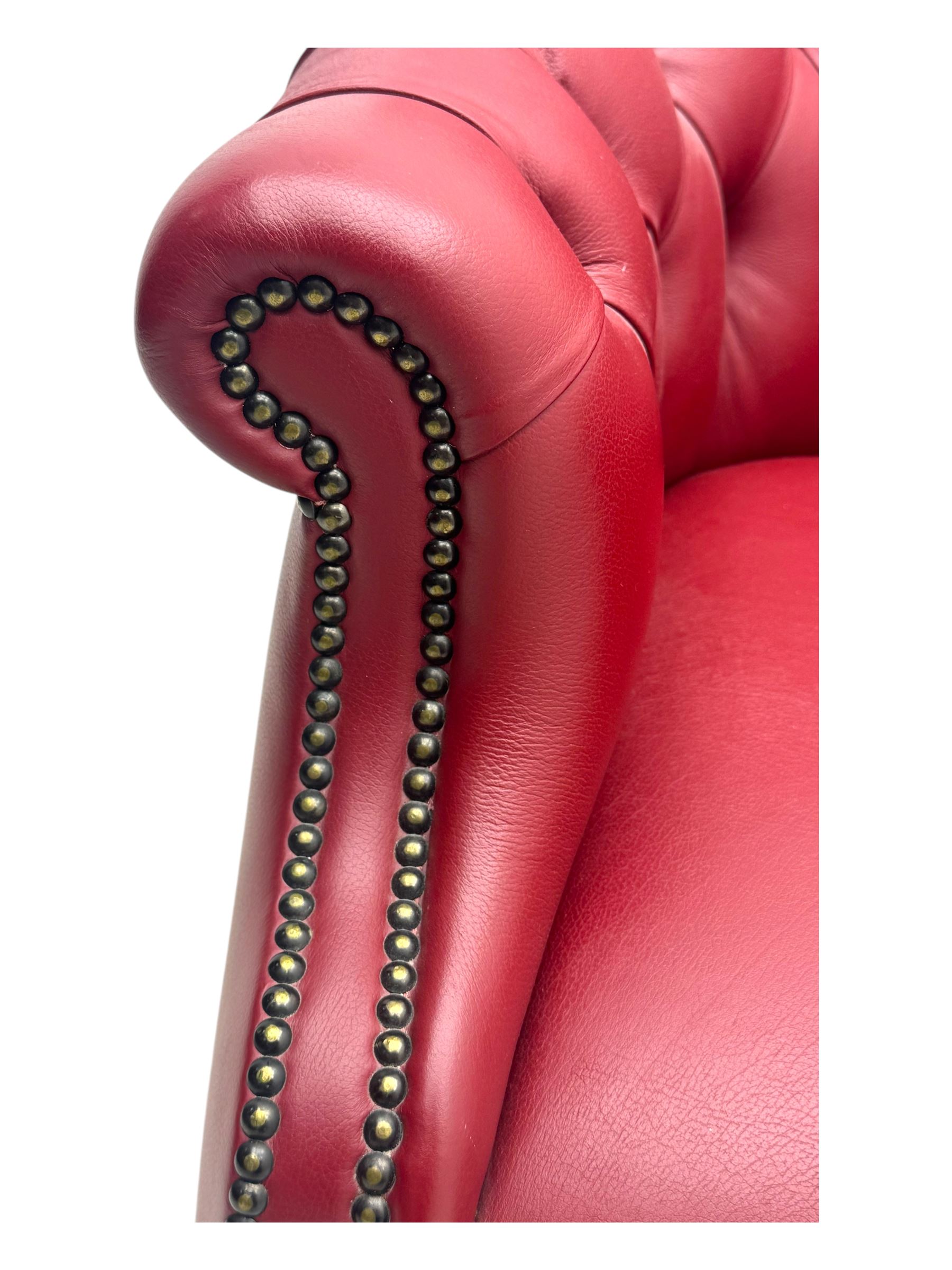 Kingsgate - contemporary 'Devon' bucket armchair, upholstered in red leather with buttoned backrest, rolled arms and brass stud detailing, raised on four dark wood supports with vertical carving