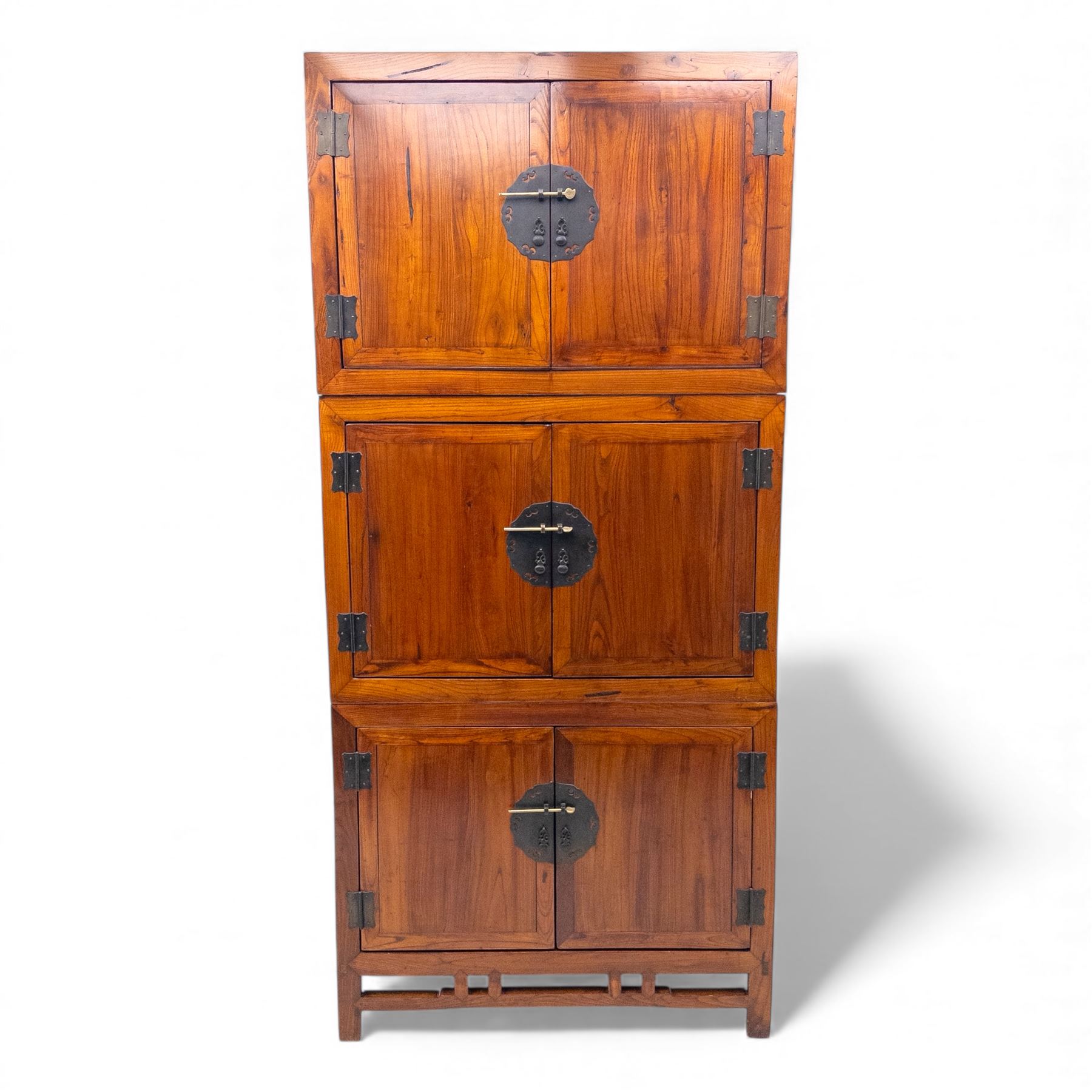 20th century Thai elm compound cabinet, formed of three stacking chests each enclosed by double panelled doors with decorative wrought metal lock plates and hinges, raised on pierced apron on stile feet