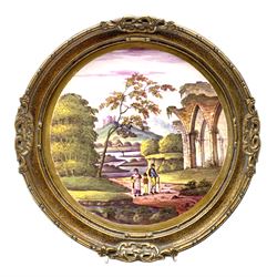19th century painted porcelain plaque, of circular form, depicting a landscape with hilltop castle in the background, river, and figures and ruin to the fore, in gilt frame, plaque D22cm overall D27.5cm