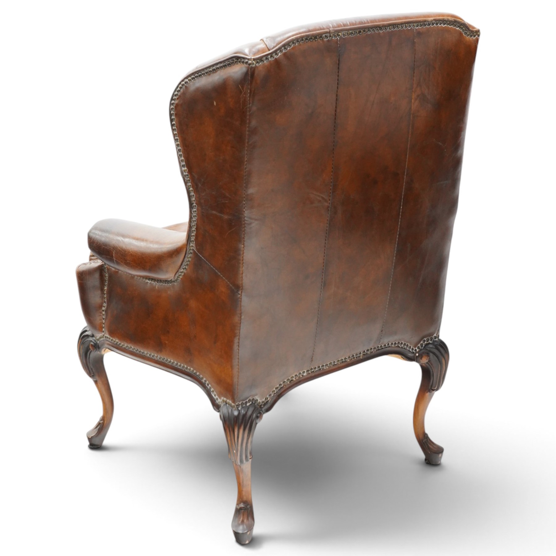 Pair of quality Queen Anne design mahogany framed wingback armchairs with matching footstools, the high sprung winged backs over rolled arms with studwork, raised on elegant reeded scroll carved cabriole supports, upholstered in deep chocolate brown leather (W82cm D75cm H112cm), the footstools with ovoid padded seat over studwork and moulded lower rail and cabriole supports (W65cm D42cm H48cm)