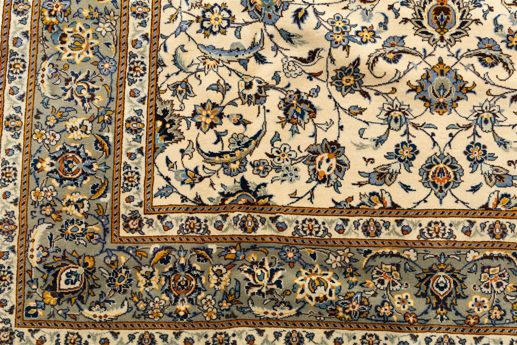 Central Persian Kashan hand-knotted rug, ivory field intricately decorated with an all-over design of scrolling vines, palmettes, and stylized lotus motifs in shades of soft blue, pale gold, and indigo within floral borders