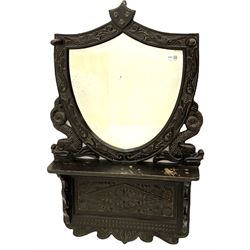 Early 20th century carved oak hall mirror, shield shaped bevelled glass plate, hat hooks, single shelf, Whitby Ammonite crest