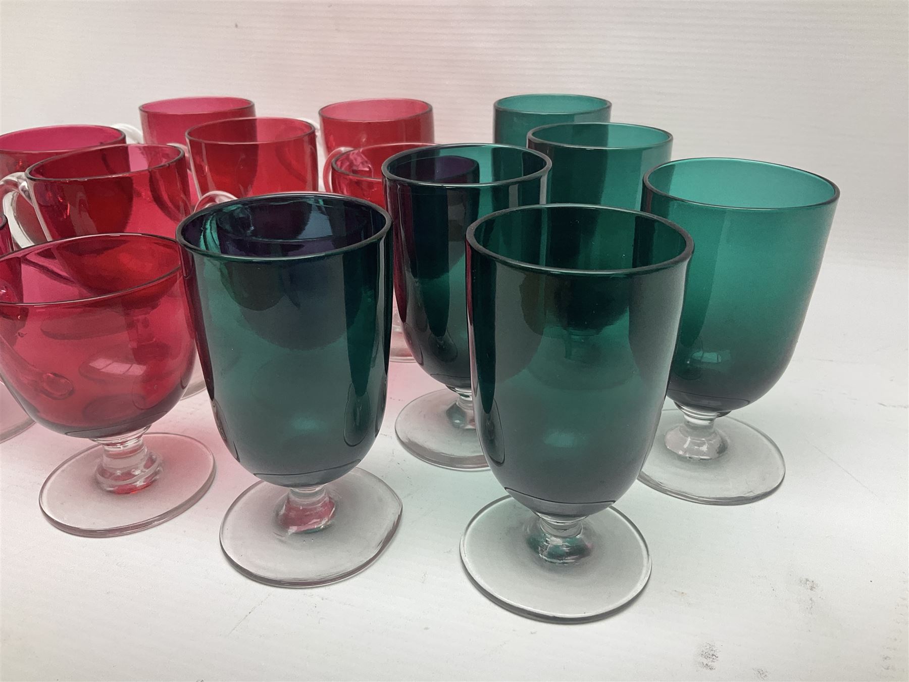 Collection of 19th century coloured glasses, to include nine cranberry glass punch cups, each with clear glass handle and foot and a set of six green glasses, with short clear stems, tallest H10cm
