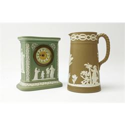 An early 20th century Wedgwood sage green jasper timepiece, decorated with classical figures and further detailed with foliate bands, with impressed marks verso, H15.5cm, together with a Paxton buff ground jasperware jug, decorated with a band of figures, H17cm. (2). 