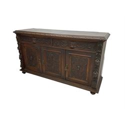 Victorian heavily carved oak sideboard, the moulded top carved with foliate decoration to the edge, fitted with two drawers and three cupboards, the drawer fronts carved with green man mask handles and scrolling foliage, the panelled doors carved with interlacing foliage, on turned compressed bun feet