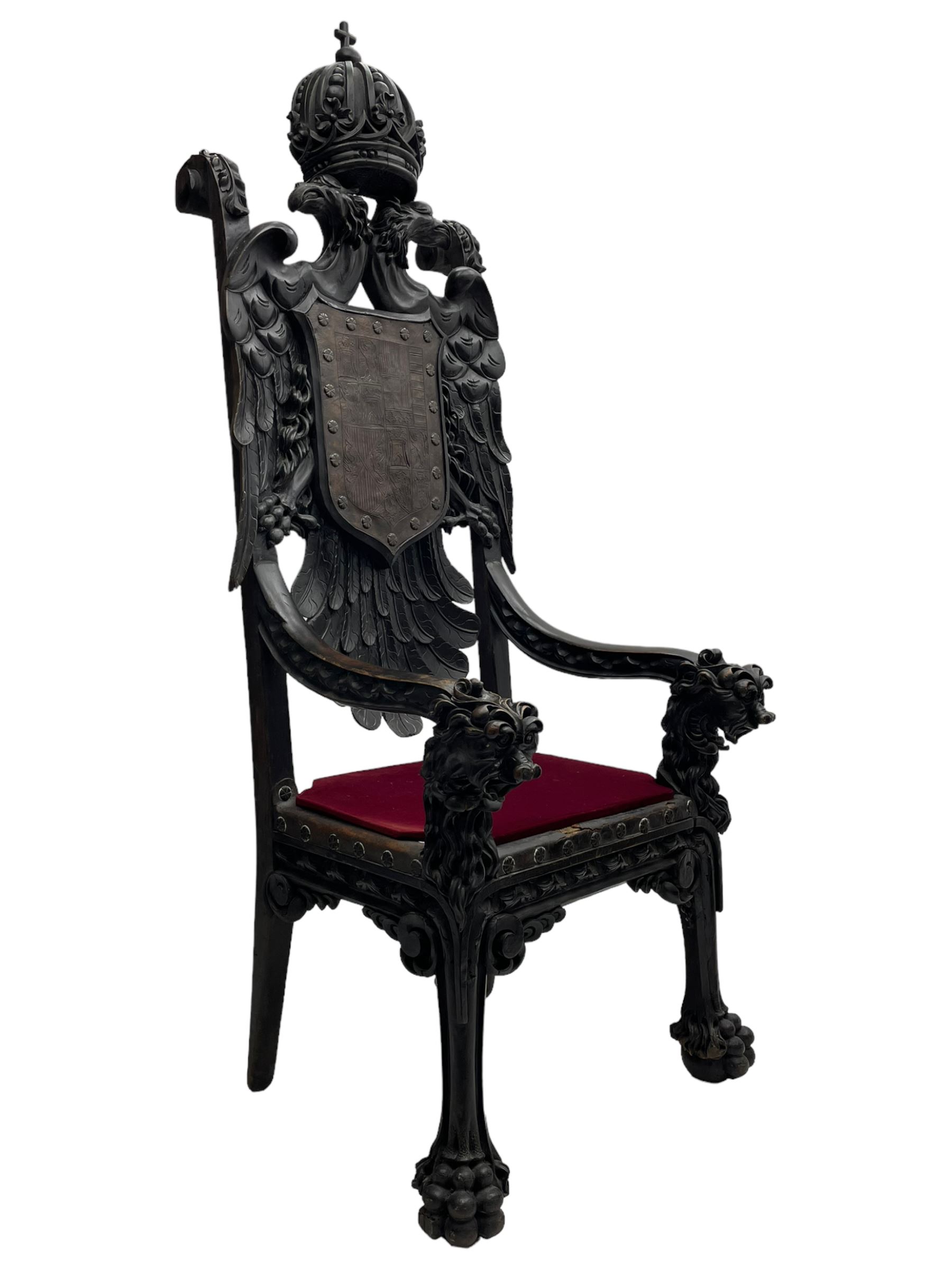 Grand mid-to-late 19th century heavily carved beech framed throne chair, the crown pediment carved with flower heads and cross finial, scroll and acanthus carved upright supports with twin perching griffin back enclosing etched leather work heraldic shield with castle and lion motifs over splayed feathers, flower head carved down sweeping arms with grotesque carved terminals, the seat rails carved with further flower heads on moulded supports with oversized ball and claw carved feet

Provenance: A very similar chair was used in the filming of Stanley Kubrick's 'Eyes Wide Shut' (1999)

