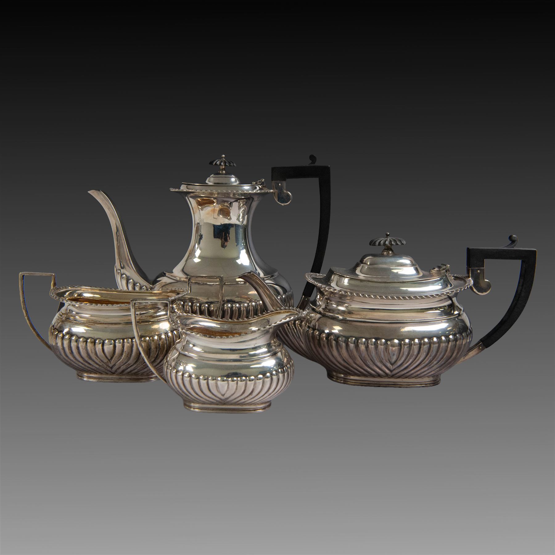 Edwardian silver four piece tea service, comprising coffee pot, teapot, twin handled open sucrier and milk jug, all of oval bellied form, part fluted and with oblique gadrooned rim, with Bakelite type handles and finials to teapot and coffee pot, hallmarked Fordham & Faulkner, Sheffield 1913