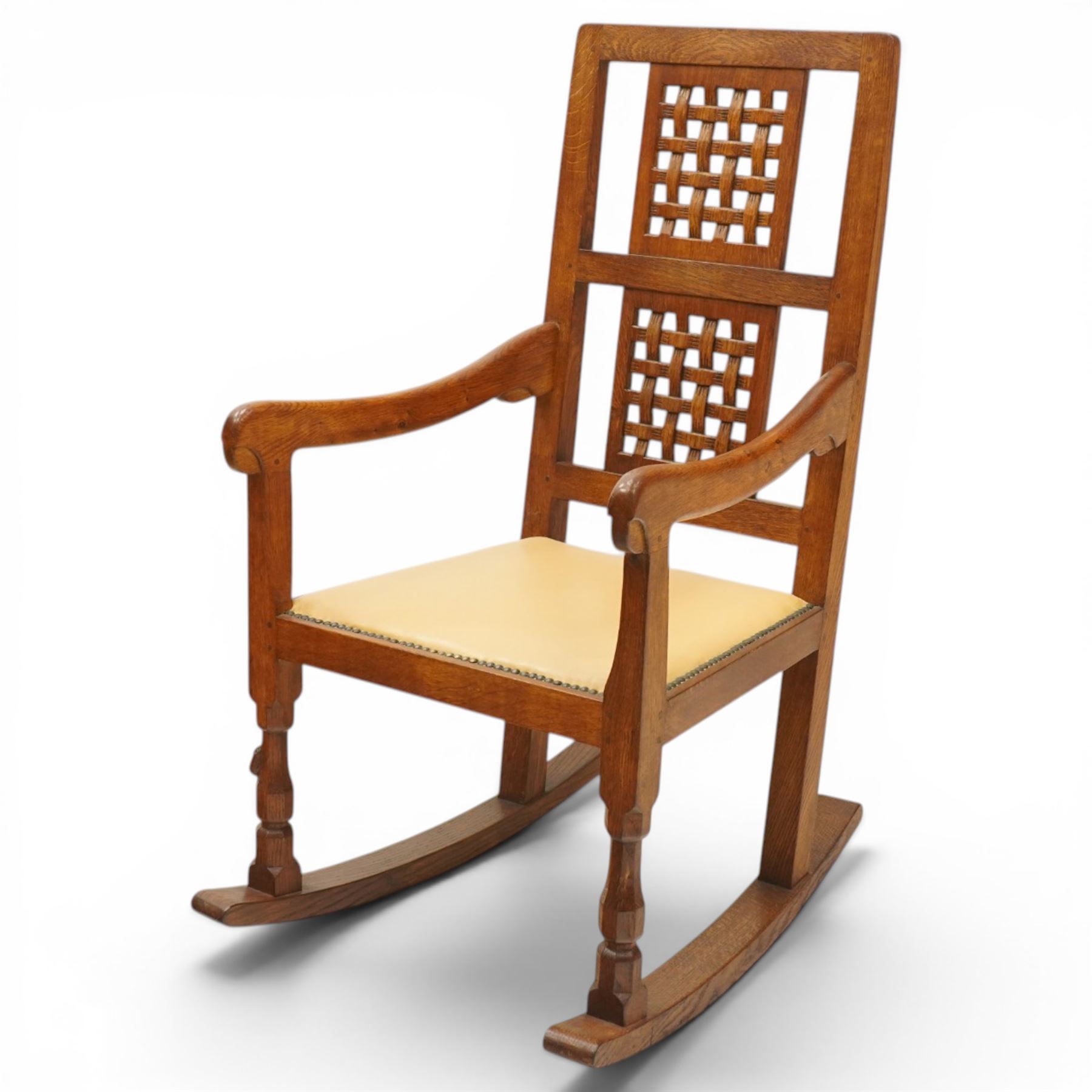 Mouseman - 1940's dark-honey oak rocking chair, high back with pierced double-lattice panel, over a beige-leather upholstered seat, shaped arm terminals above turned octagonal front-supports united by rocker base, with carved mouse signature, by the workshop of Robert Thompson of Kilburn