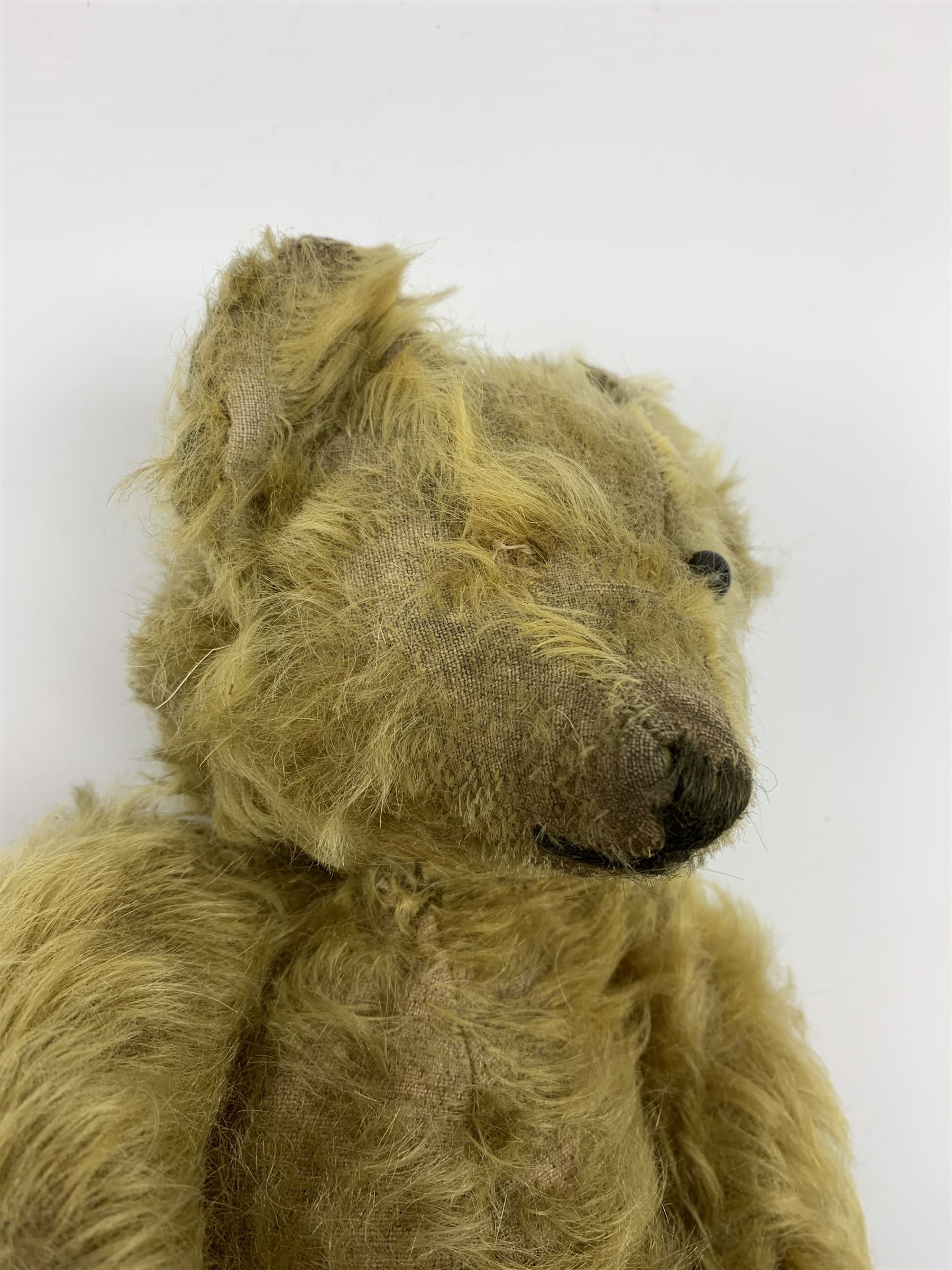 Early 20th century English teddy bear, WW1 period, with wood wool filled mohair body, fixed head with one boot button eye and vertically stitched nose and mouth and jointed limbs with cloth paw pads H16