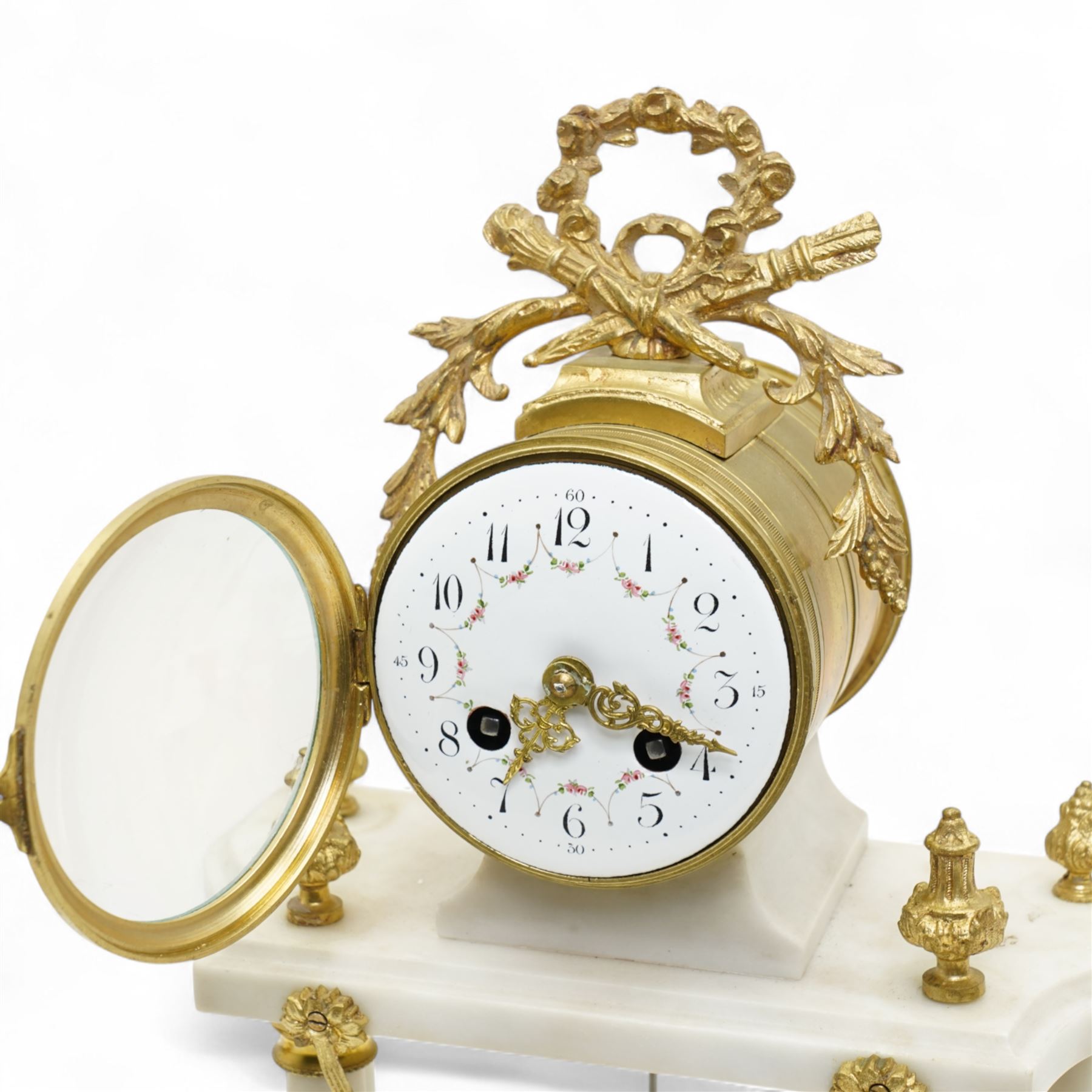 French-Early 20th century 8-day white marble and gilt metal striking portico mantle clock and garniture, Parisian drum movement with a white enamel dial, Arabic numerals and garland swags, two train countwheel striking movement sounding the hours and half hours on a bell. With a matching pair of conforming urns with gilt mounts. 