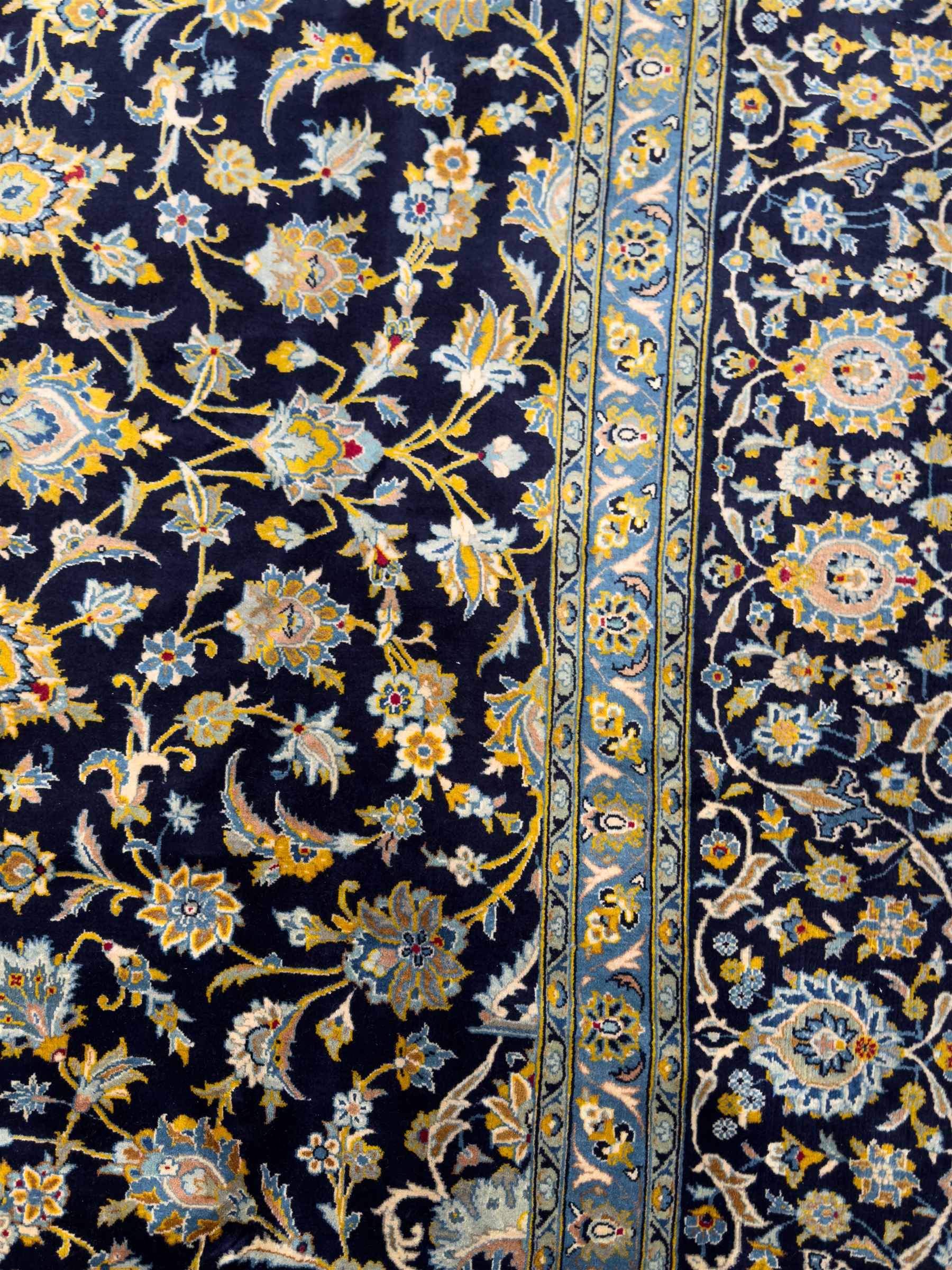 Central Persian Kashan hand-knotted carpet, the navy field with central medallion in pale blue and gold tones, surrounded by spiralling arabesques and palmettes, framed by quarter spandrels and a wide border of stylised lotus and rosette motifs between floral guard stripes, from the region of Kashan