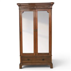Edwardian walnut double wardrobe, featuring two mirrored doors with bevelled plates, carved frieze with fluted pilasters, above single base drawer