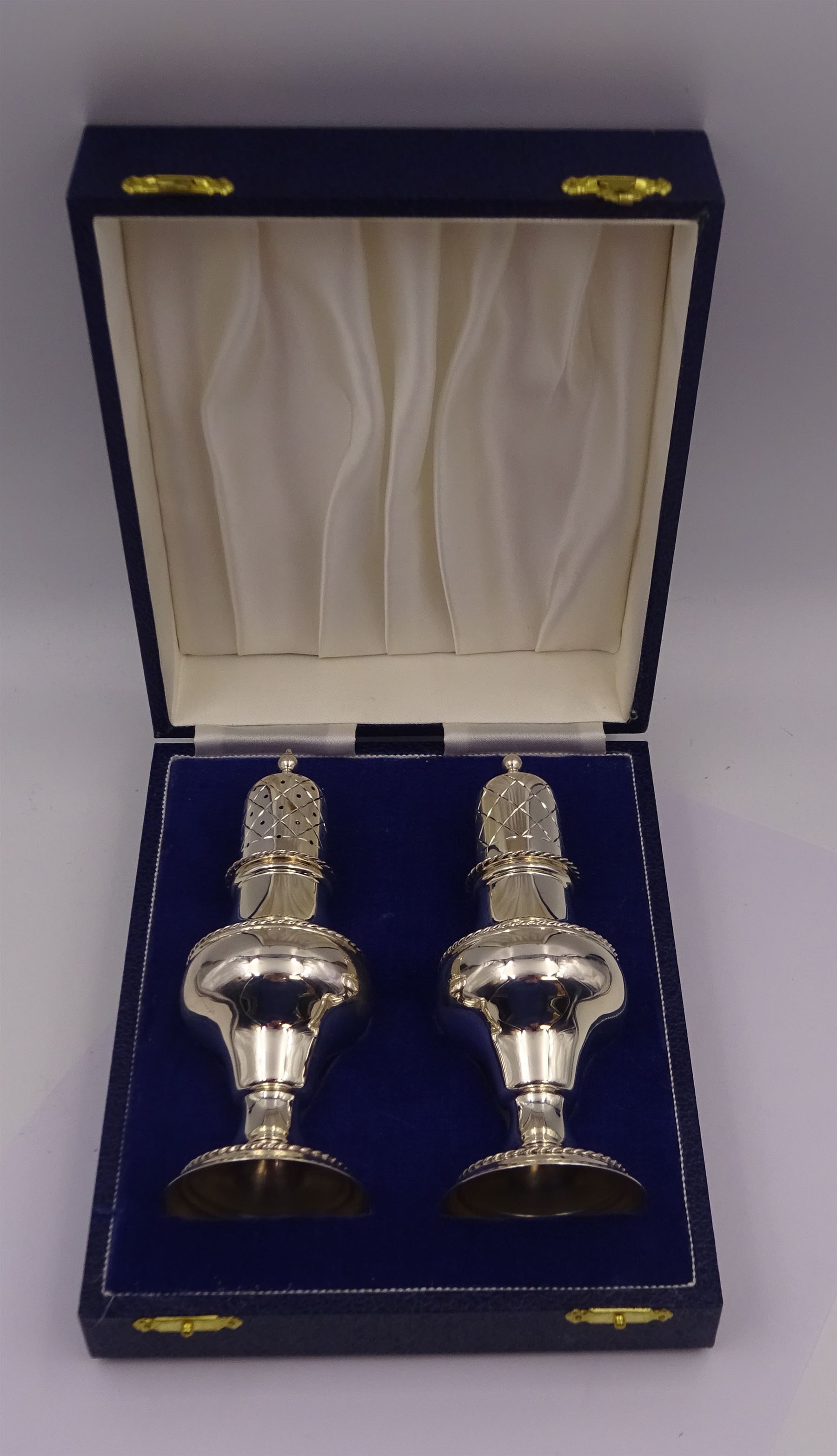 Modern silver two piece cruet set, comprising salt shaker and pepper shaker, both of waisted form with engraved rope twist borders, the removable pierced covers each with engraved lattice decoration, upon a circular spreading foot, hallmarked Laurence R Watson & Co, Birmingham 1989, H14.5cm, contained within velvet lined fitted case