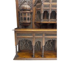 Late 19th century Indian Burmese carved and pierced hardwood and brass inlaid wall shelf, the shaped back profusely decorated with trailing and interlaced foliage, with projecting architectural structures, the central balcony with canopy top and five open windows with arched apertures on columns, two flanking five-sided balconies, the shelf supported by six foliate carved columns with pierced cusped pointed arches 