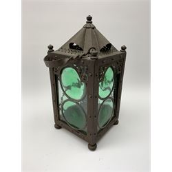 An Arts & Crafts wrought iron lantern, of square sided form with swing handle, and green and clear glass panels, raised upon four compressed bun feet, not including handle H30.5cm.