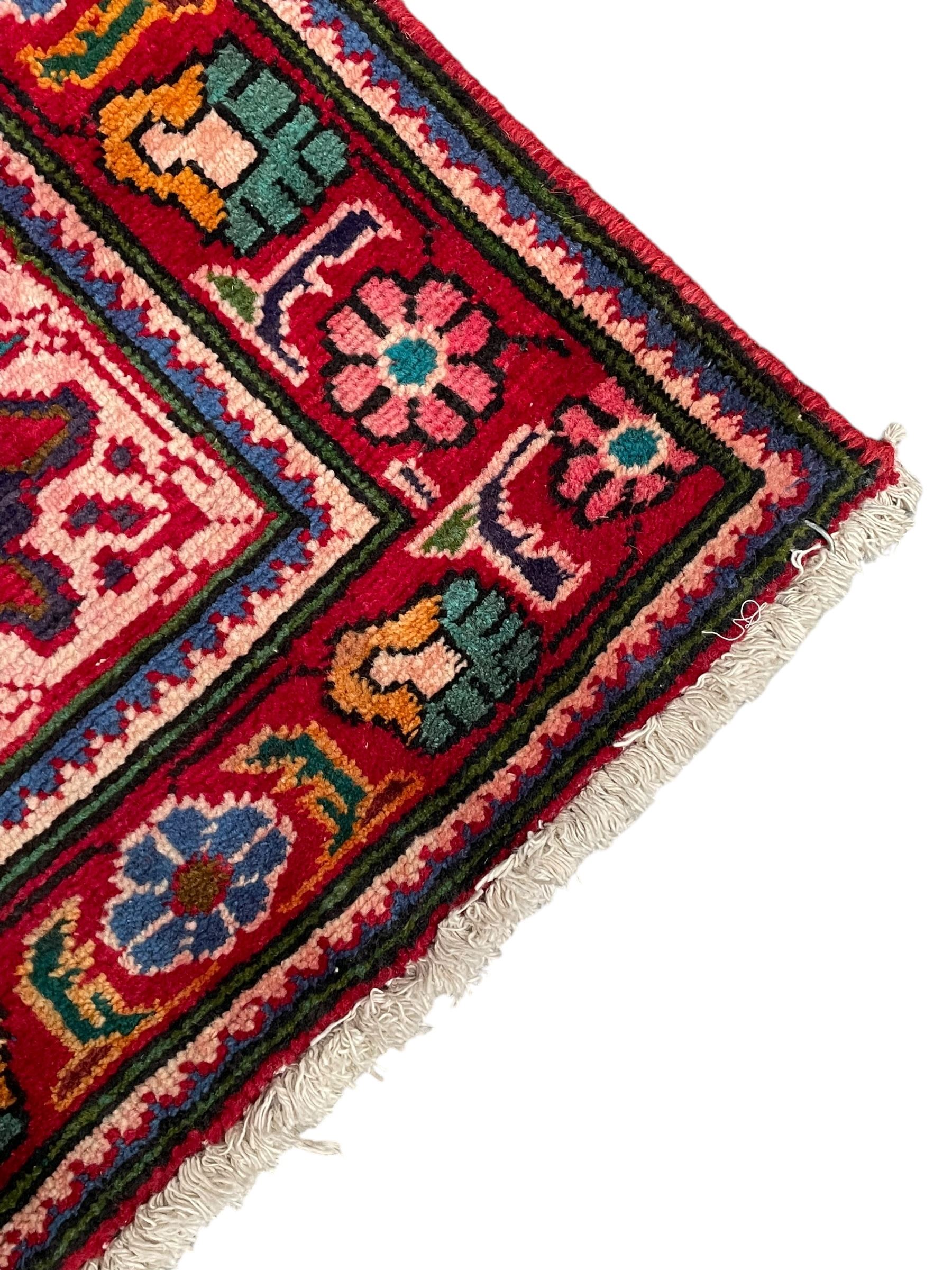 Persian Azerbaijan crimson ground rug, the field decorated with central floral motif and surrounded by trailing floral branches, enclosed within a shaped outer band with further floral decoration, the border with repeating flower heads, geometric guard stripes 