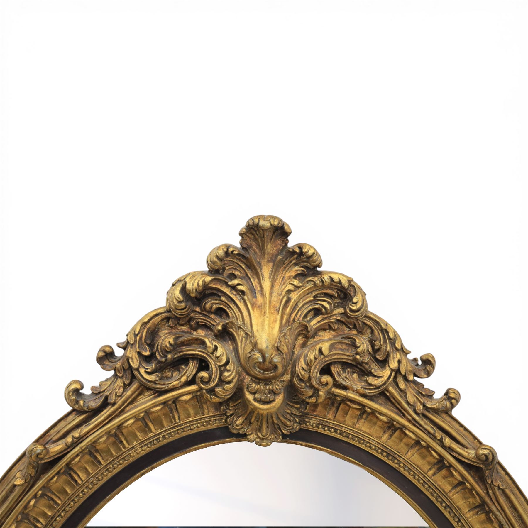 Rococo Revival style gilt composition oval wall mirror, moulded oval frame with fluted and beaded bands enclosing a bevelled mirror plate, the outer frame with acanthus leaf and scroll carved cresting to each side