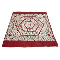 19th century patchwork quilt, hand stitched from hexagons of various materials including printed patterned and floral examples, featuring repeating large central hexagon to centre, the top and bottom with thick panel red jacquard border, the sides bordered with plain red fabric, lined with panels to reverse, 180 x 190 cm