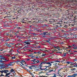 Large North East Persian Meshed hand-knotted carpet with signature, raspberry red field with central shaped cusped medallion, densely decorated with intricate arrangement of scrolling vines, and florals designs within conforming spandrels and a dark ground border richly ornamented with stylized flowers, vase and bird ornamentation, enclosed by guard stripes, with cotton fringe ends