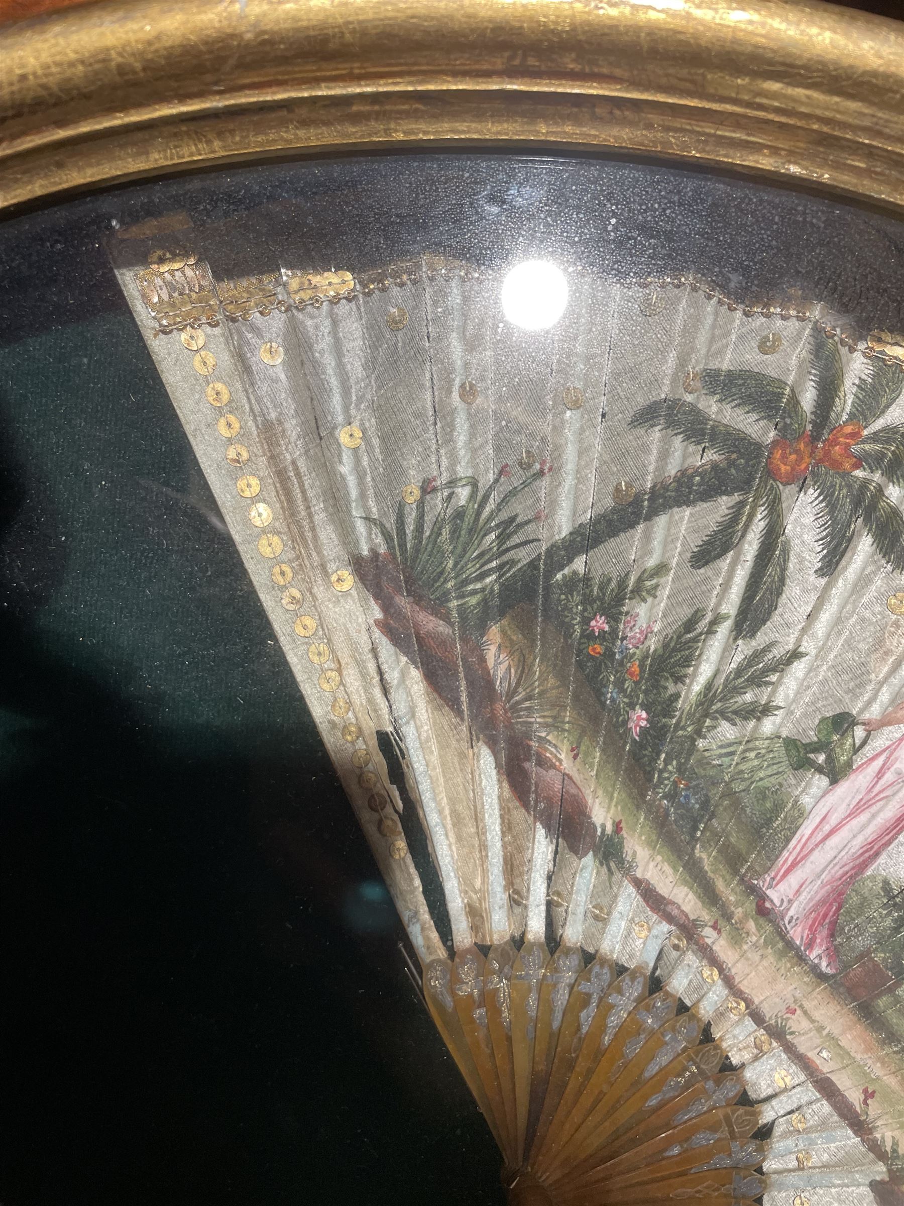 18th century fan, the horn sticks and guard with silvered and gilded decoration, the silk leaf painted in strong colours with a young couple in a garden setting, within a border of gold coloured sequins, framed and glazed, overall H35cm L55cm
Provenance: From the Estate of the late Dowager Lady St Oswald