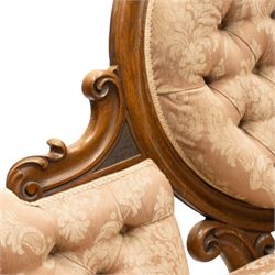 Victorian carved walnut framed double-ended settee with serpentine front, the central oval cameo back with flowerhead carved cresting rail, flanked by foliate C-scroll spandrels, the scroll carved arm terminals over floral carved cabriole supports with scroll feet and ceramic castors, the buttoned back and sprung seat upholstered in pale pink foliate patterned damask fabric
