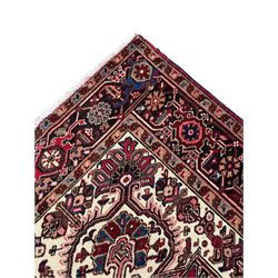 Persian Heriz red ground rug, central scrolled medallion on dark ground decorated with floral motifs, the surrounding field decorated with stylised plant motifs and smaller geometric symbols, guarded border with repeating pattern punctuated with rosettes and flower heads 