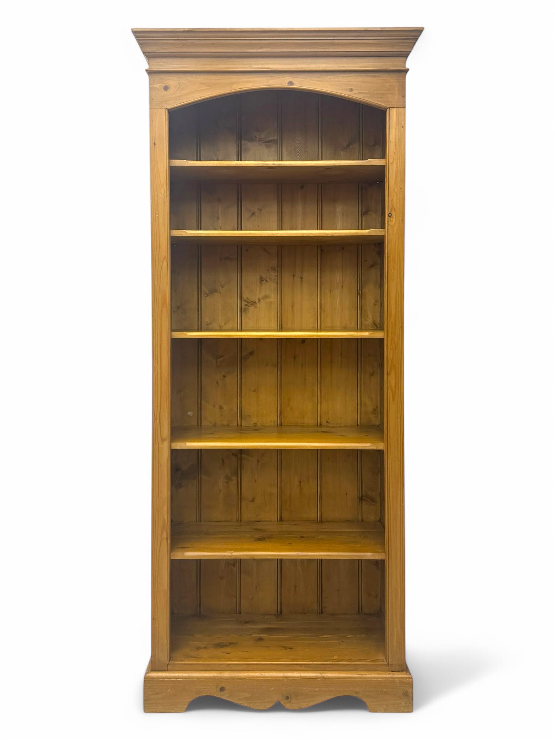 Early 20th century pine bookcase, projecting cornice over arched open shelving area with five adjustable shelves, on shaped plinth base