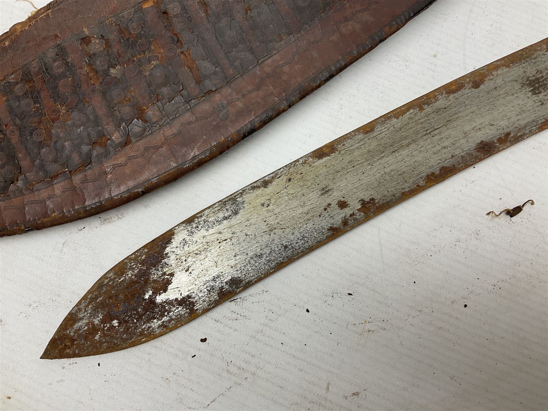 Mandingo sword, the 63cm plain curving steel blade marked with a horses head and the initials G.S.; leather covered grip with metal ribbed spherical pommel; in decorative leather leaf scabbard mounted with tassels and roundels L84cm overall; and a North African flyssa sword in poor condition with wooden scabbard (2)
