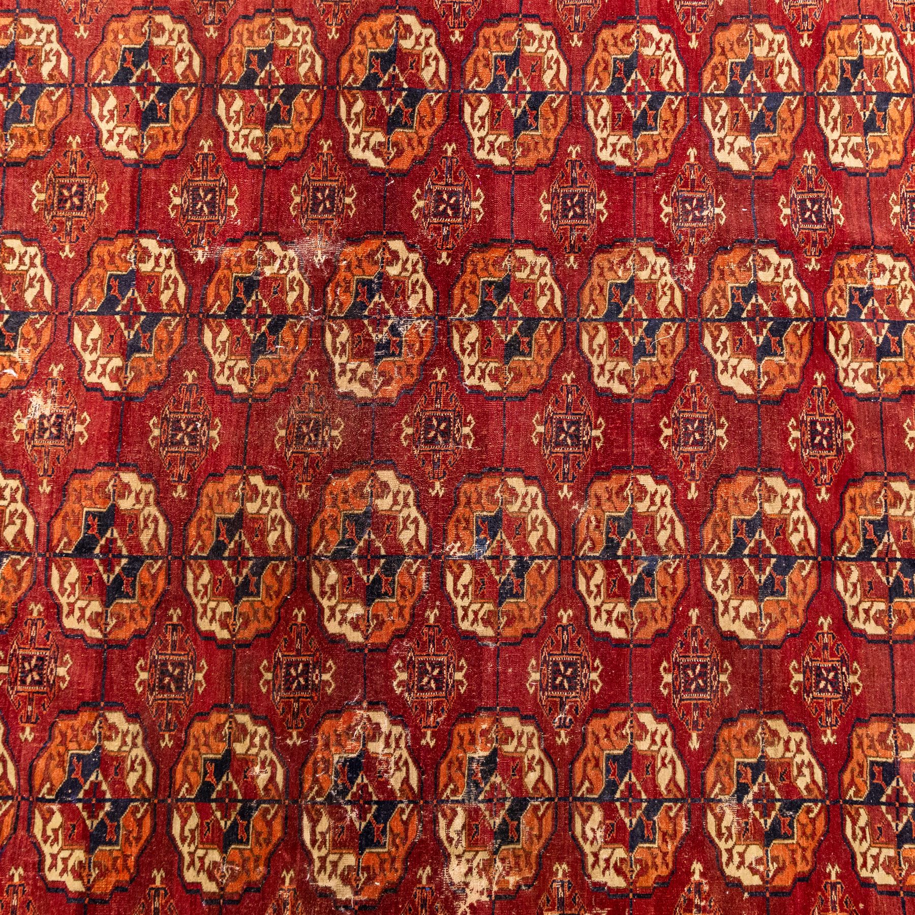 Vintage Bokhara hand-knotted rug, madder field woven in rows of octagonal Tekke guls arranged in vertical columns, each enclosing angular cruciform devices and tribal motifs, divided by narrow indigo lines, within multiple geometric borders incorporating stepped lozenges and latch hook devices, with cotton fringe ends 