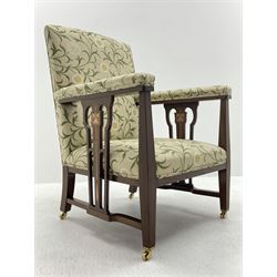 Late 19th century Arts and Crafts mahogany armchair, upholstered in a pale ground fabric decorated with trailing foliage and flower heads, pierced splats to each side with stylised flower inlay, square tapering supports, brass castors