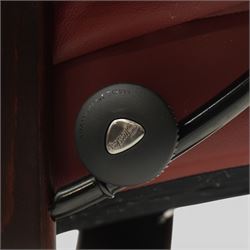 Ekornes - Stressless reclining armchair and matching footstool, upholstered in oxblood leather with padded headrest and segmented back cushion, shaped armrests with exposed adjustment handles, raised on stained laminated beech circular swivel base, the conforming stool on matching ring base