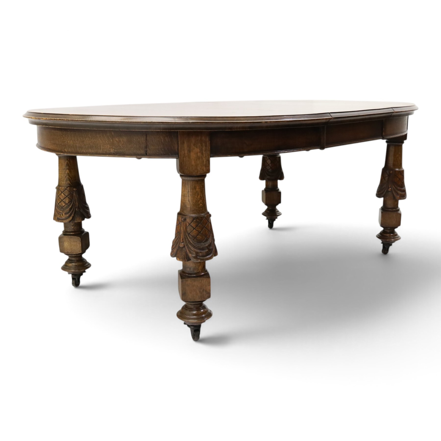 Late 19th century French oak extending dining table, oval top with moulded edge and plain frieze, raised on four ornate carved supports decorate with carved latticework and large festoons with tassels, on turned feet, with two additional leaves