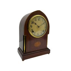 A late 19th century American  mantle clock in a “Lancet” case manufactured by the  Gilbert Clock Factory, Connecticut,  mahogany veneered case with an oval inlay, satinwood stringing to the edge and two recessed brass pillars, on a moulded plinth with four bun feet, enamel dial with upright Arabic numerals and spade hands, fast/slow regulation, with a convex glass and spun brass bezel, eight-day movement striking the hours and half hours on a coiled gong. No pendulum.