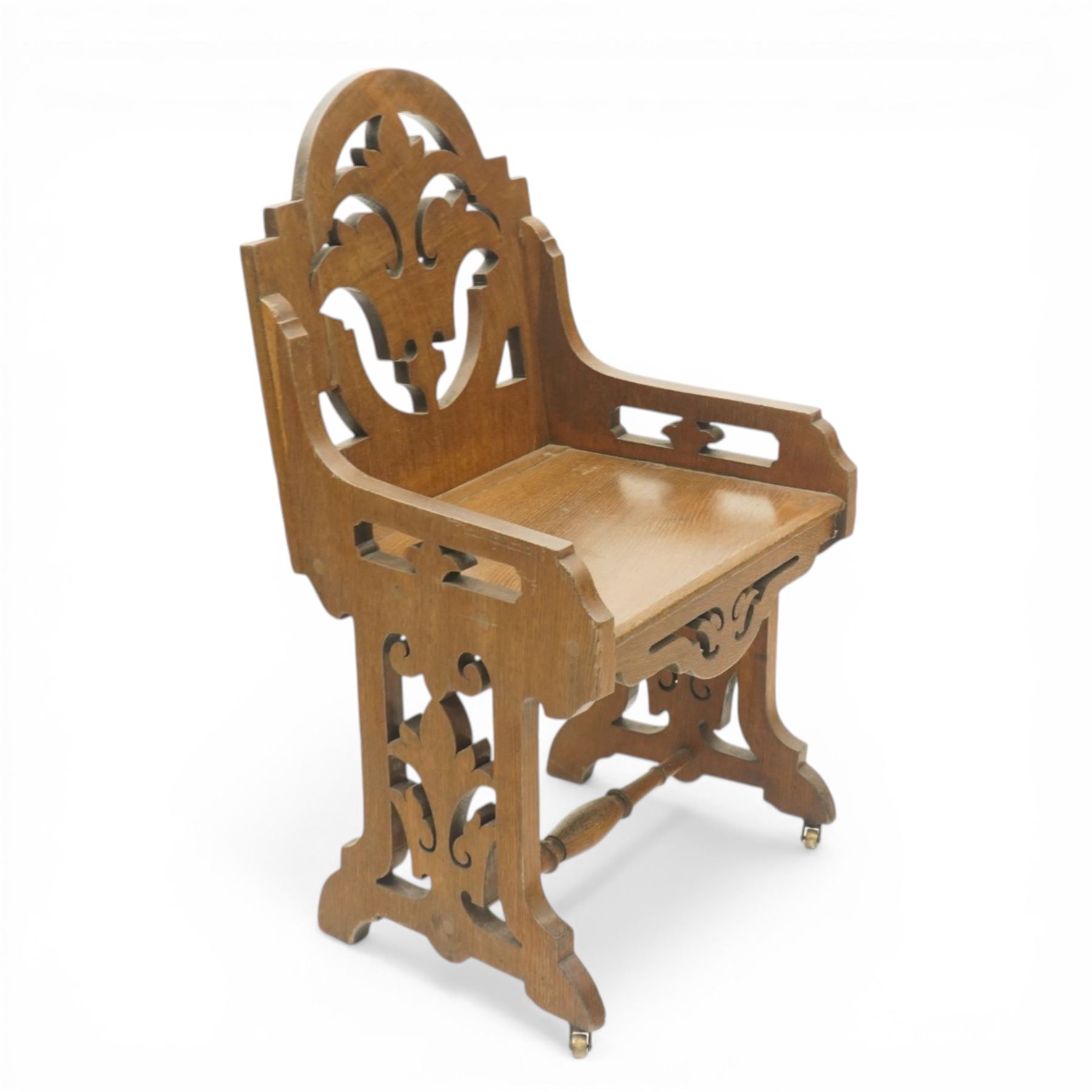 Gothic Revival oak ecclesiastical chairs, shaped cresting rails over pierced foliate splat backs, plank seats above shaped and pierced friezes, raised on shaped end supports united by turned stretchers, on small brass castors