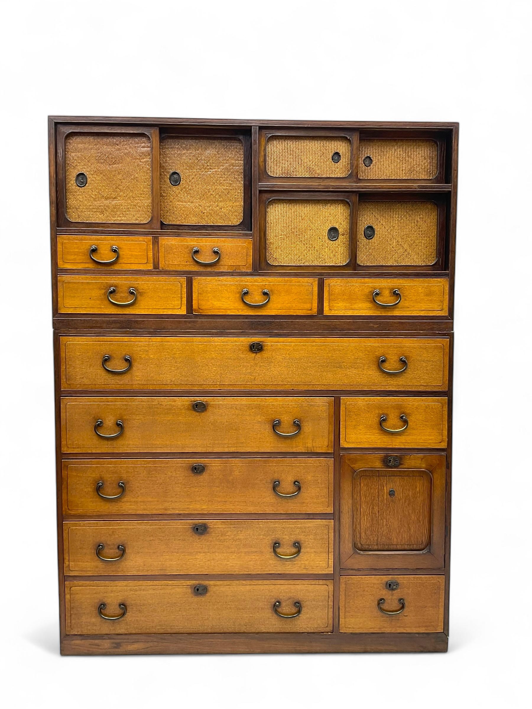 Late Meiji-period Japanese keyaki wood tansu chest, upper section with six sliding woven rattan doors over five drawers, lower section fitted with an asymmetrical arrangement of seven drawers and side cupboard with a hinged door enclosing three additional drawers, iron drop handles to sides