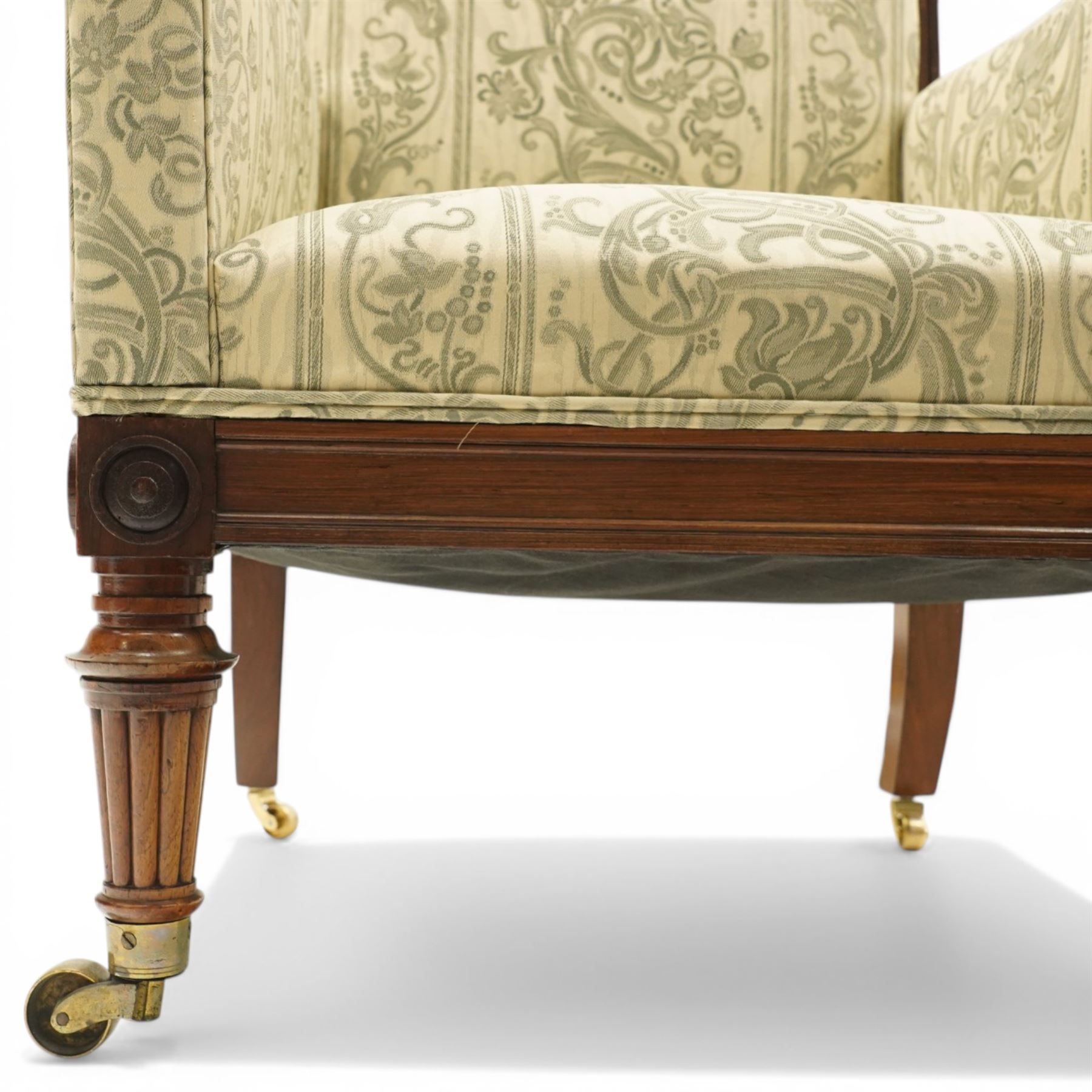 William IV rosewood framed library armchair, squared form with green on ivory ground upholstery, moulded lower seat rail with applied roundels over reeded supports, terminating to brass cups and castors